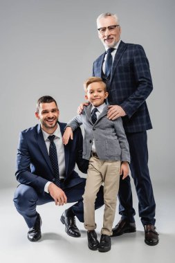 happy businessmen with boy in formal wear smiling at camera on grey clipart