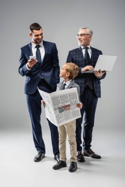 Babam ve büyükbabamın yanında gazetesi olan gülümseyen bir çocuk gri üzerinde aletler tutuyor.