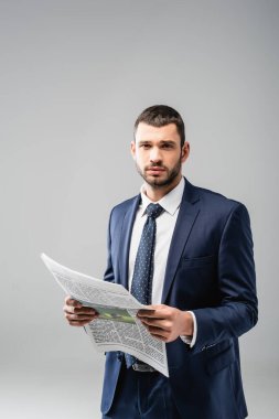 Gri üzerine gazete tutarken kameraya bakan düşünceli işadamı.