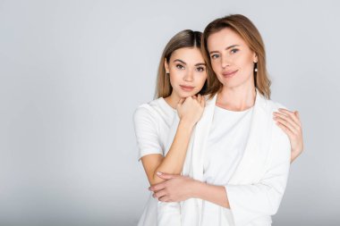 Genç kız, mutlu anneye sarılıyor. Gri kuşak kadınların üzerinde. 