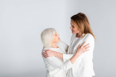 Büyük anne ve mutlu kız birbirlerine bakıyorlar. Gri renkte birbirlerine sarılıyorlar. 