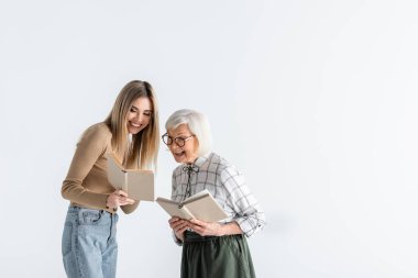 Beyaz gözlüklü büyükanneyle kitap okuyan mutlu genç bir kadın.