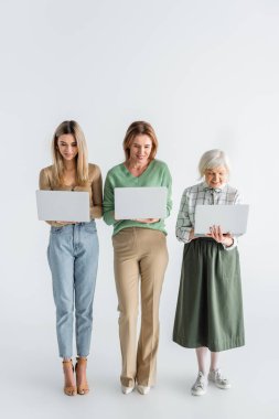 Beyaz dizüstü bilgisayar kullanan üç nesillik mutlu kadınların tam uzunluğu