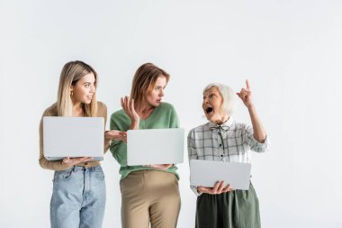 Anne ve küçük kızı dizüstü bilgisayar tutuyor ve beyaz parmak gösteren yaşlı kadına bakıyor.