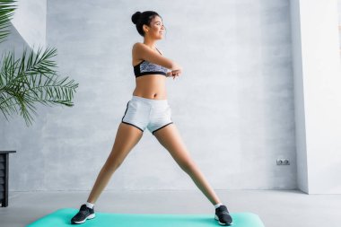Afro-Amerikalı bir kadının evde spor paspası üzerinde ısınma egzersizi yapmasını uzun süre izlemek.