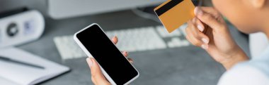 Afrika kökenli Amerikalı bir kadının kredi kartı ve akıllı telefonu elinde boş ekran, pankart tutarken kısmi görüntüsü