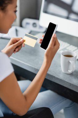 Beyaz ekran ve kredi kartıyla akıllı telefon tutan Afro-Amerikan kadının görüntüsü bulanık.