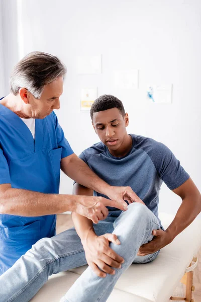 アフリカ系アメリカ人患者の膝を指差す成熟したカイロプラクター — ストック写真