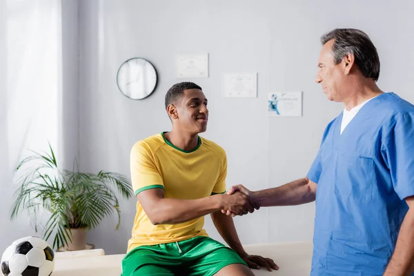 快乐的非洲裔美国足球运动员在诊所与医生握手 — 图库照片