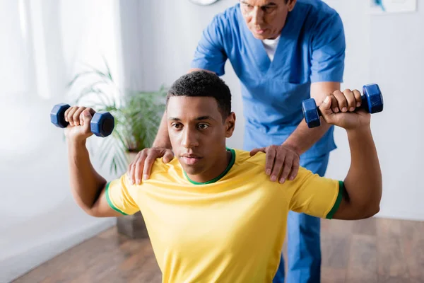 Afro Americano Desportista Exercitando Com Halteres Perto Fisioterapeuta Fundo Turvo — Fotografia de Stock