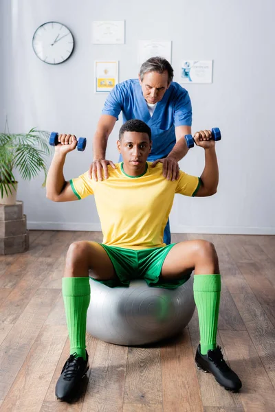 Entrenamiento Deportista Afroamericano Con Pesas Pelota Fitness Cerca Fisioterapeuta Durante —  Fotos de Stock