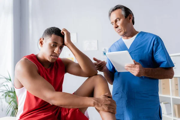 Chiropraktiker Hält Digitales Tablet Der Nähe Verärgerter Afroamerikaner Sportbekleidung Klinik — Stockfoto