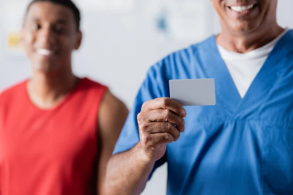 Alegre Médico Sosteniendo Tarjeta Blanco Cerca Africano Americano Paciente Ropa — Foto de Stock