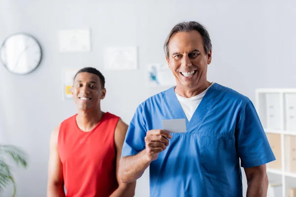 Doctor Feliz Sosteniendo Tarjeta Blanco Cerca Del Paciente Afroamericano Ropa —  Fotos de Stock