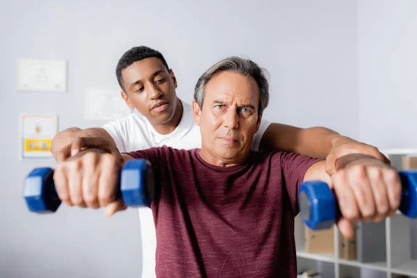 Afrikansk Amerikansk Fysioterapeut Hjälper Medelålders Man Tränar Med Hantlar Suddig — Stockfoto