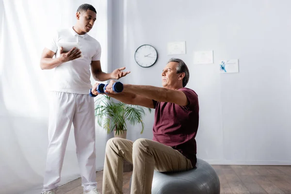 Homem Meia Idade Exercitando Com Halteres Bola Fitness Perto Fisioterapeuta — Fotografia de Stock