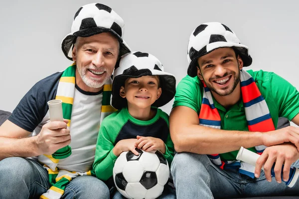 happy boy with soccer ball watching football championship together with dad and grandfather isolated on grey