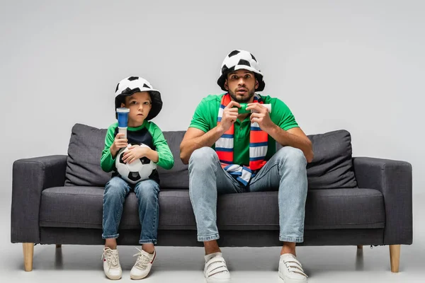 Angespannter Vater Und Sohn Mit Fanhüten Sehen Fußballspiel Auf Grau — Stockfoto