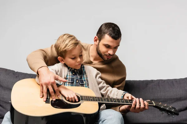Pai Ensinando Filho Tocando Guitarra Acústica Enquanto Sentado Sofá Isolado — Fotografia de Stock