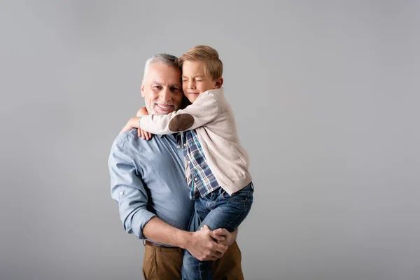 明るい男がカメラを見ていると孫が彼を抱きかかえている間灰色に隔離された目で — ストック写真