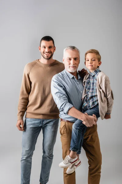 幸せな成熟した男灰色に隔離された陽気な息子の近くに孫を保持 — ストック写真