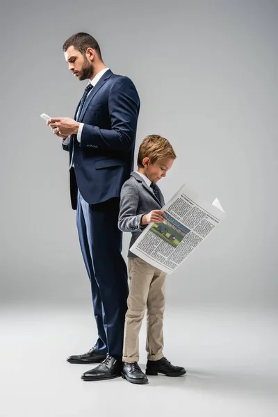 Businessman Messaging Smartphone While Standing Back Back Son Reading Newspaper — Stock Photo, Image