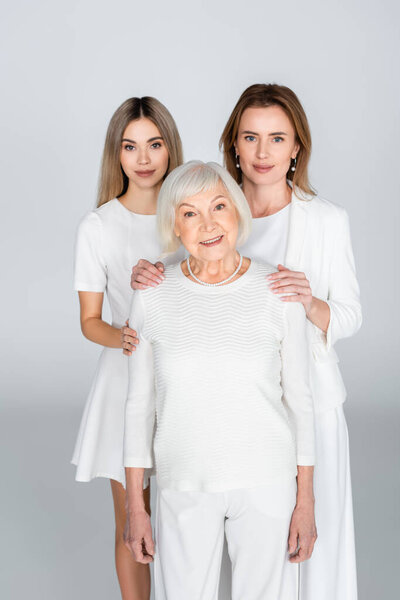 mother and daughter near smiling grandma on grey, generation of women 