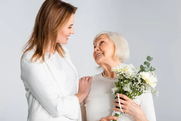 Figlia Allegra Guardando Felice Madre Anziana Con Fiori Isolati Grigio — Foto Stock