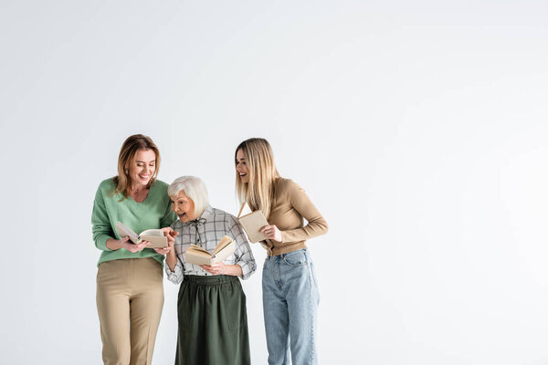 three generation of happy women holding books and smiling isolated on white