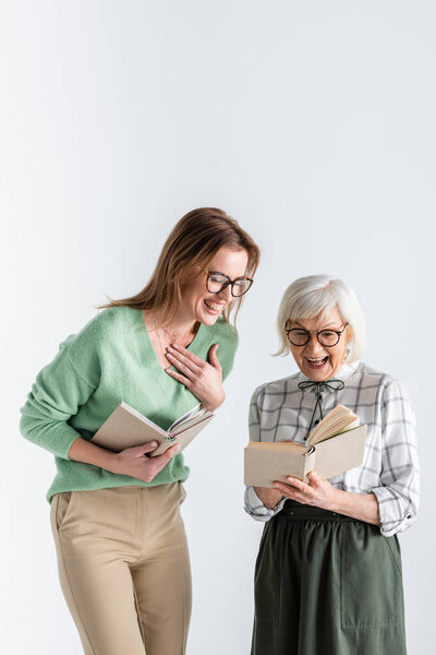 senior woman laughing with daughter in glasses while holding books isolated on white