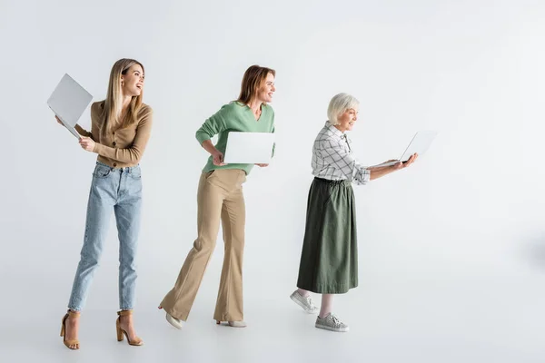 Longitud Completa Tres Generaciones Mujeres Alegres Sosteniendo Computadoras Portátiles Blanco —  Fotos de Stock