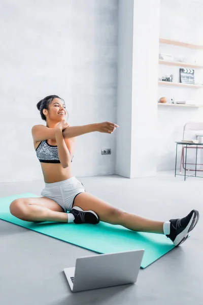 Mujer Afroamericana Feliz Estiramiento Estera Fitness Cerca Computadora Portátil Casa — Foto de Stock