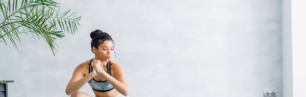 young african american woman in sports bra warming up at home, banner