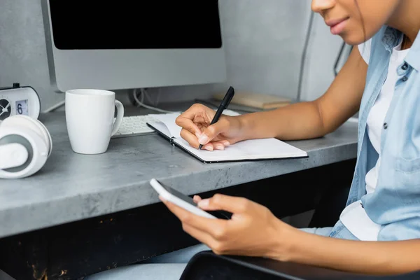 Vista Cortada Freelancer Afro Americano Usando Telefone Celular Escrita Notebook — Fotografia de Stock