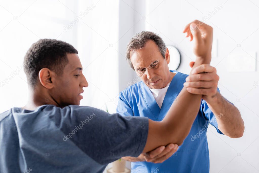 therapist working with injured african american man on blurred foreground in clinic 