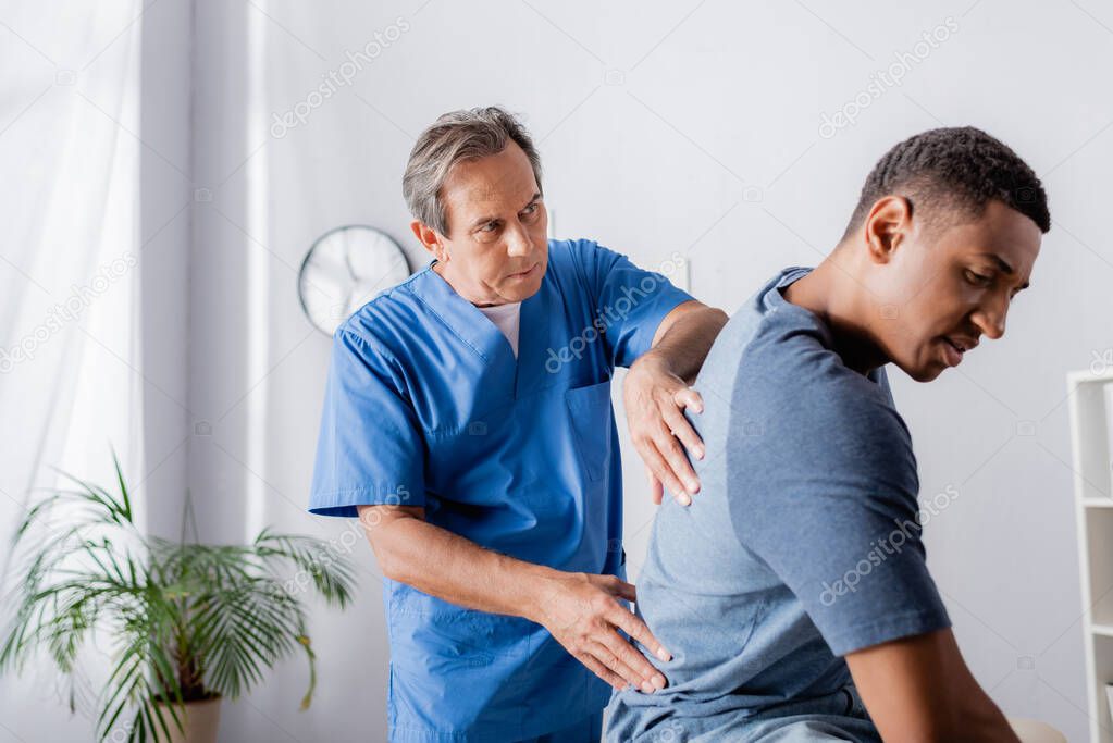 mature chiropractor working with young african american man 