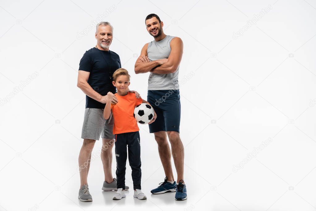 happy grandfather touching shoulders of boy holding soccer ball near man standing with crossed arms on white