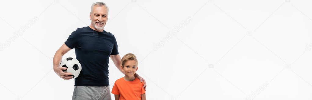 cheerful man holding hand on shoulder of grandson while holding soccer ball isolated on white, banner