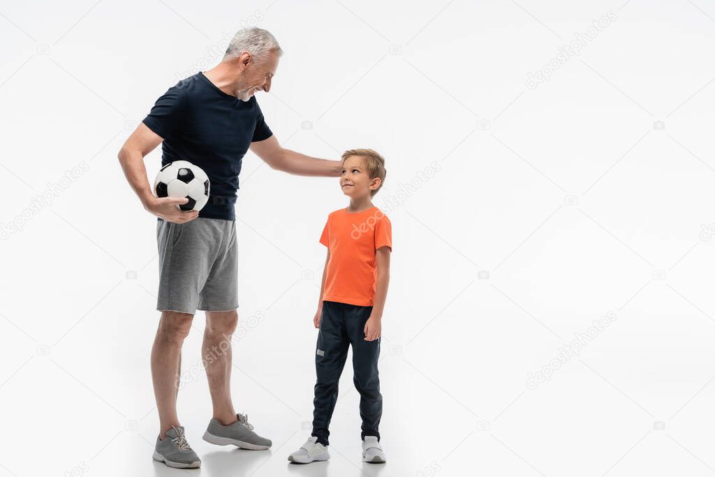 happy grandfather touching head of smiling grandson while holding soccer ball on white