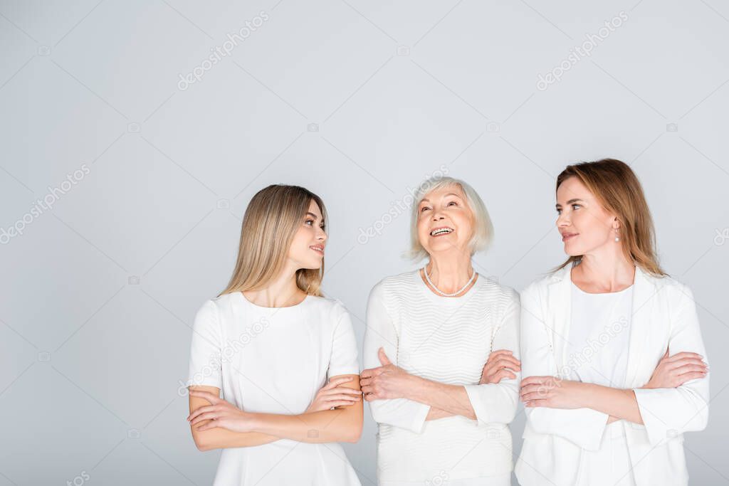 three generation of happy women standing with crossed arms isolated on grey
