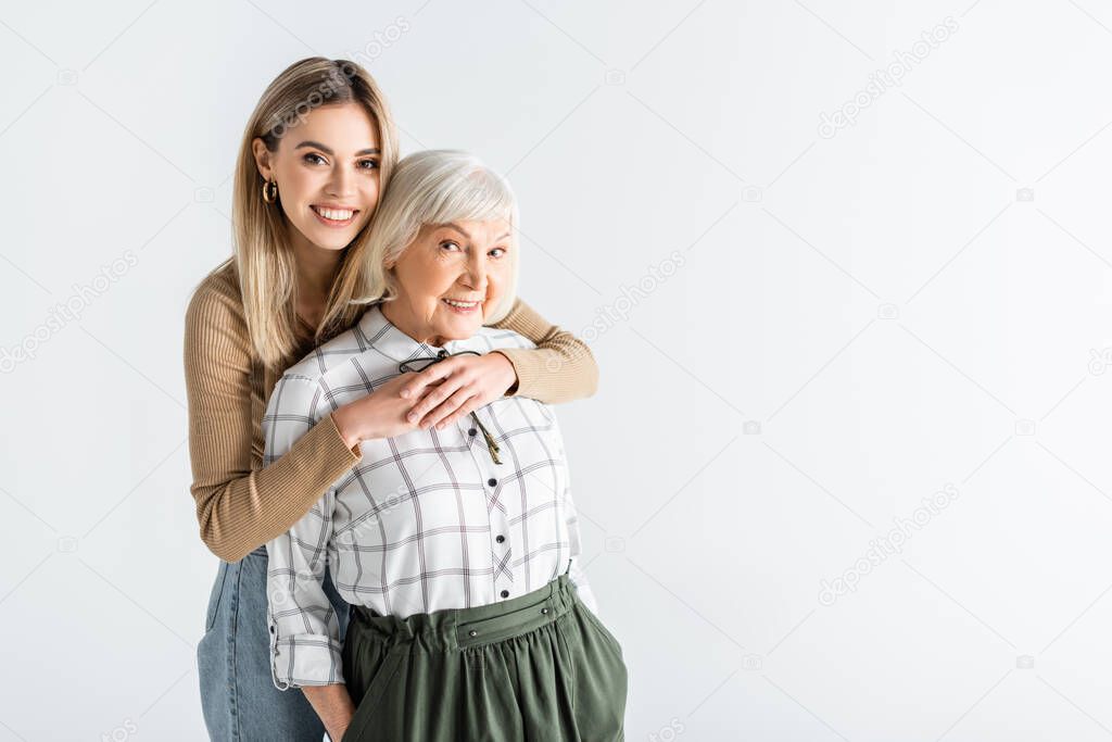 cheerful granddaughter hugging senior granny isolated on white