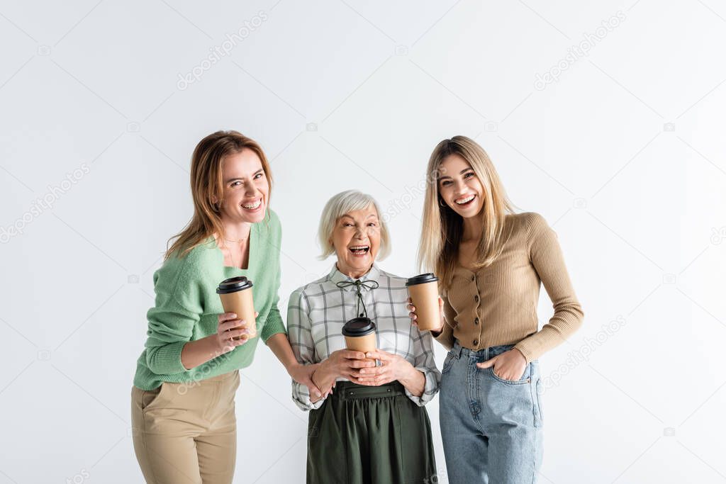 three generation of cheerful women holding paper cups isolated on white