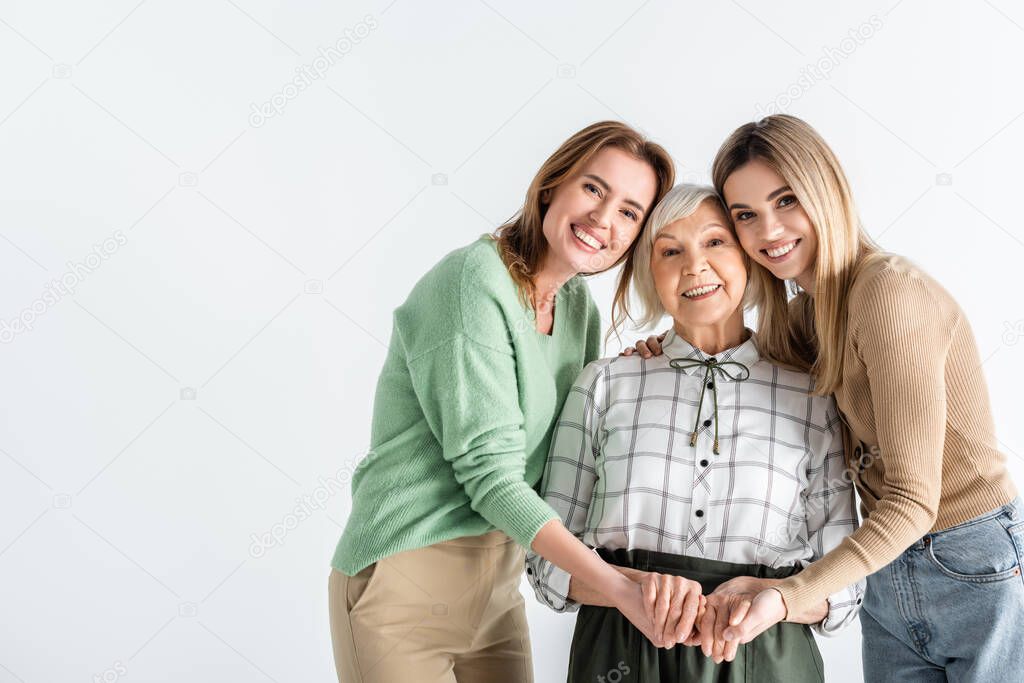 three generation of happy women looking at camera and holding hands isolated on white