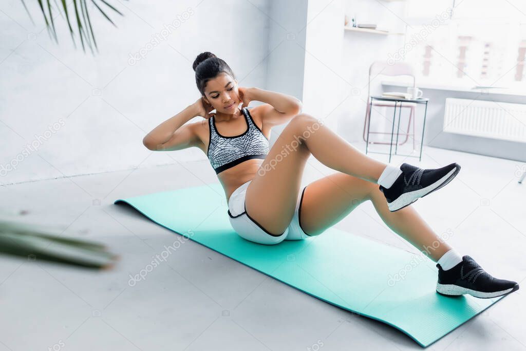 african american woman in sportswear doing abs exercise on fitness mat, blurred foreground