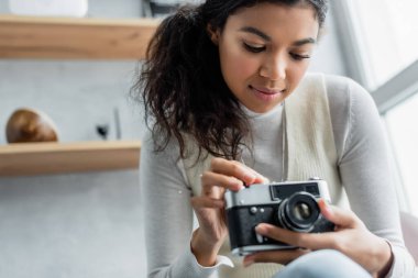 Genç Afrikalı Amerikalı kadın bulanık ön planda klasik fotoğraf makinesini ayarlıyor.