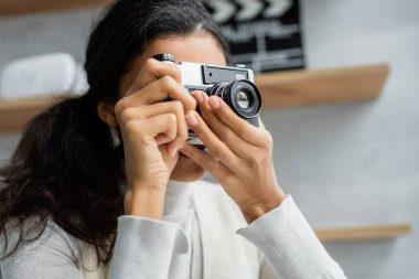 Genç Afro-Amerikalı kadın evde eski model fotoğraf makinesiyle fotoğraf çekiyor.