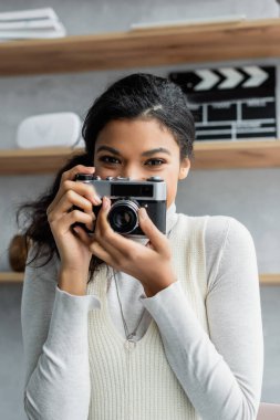 Pozitif Afro-Amerikalı kadın evde eski model kamerayla fotoğraf çekiyor.