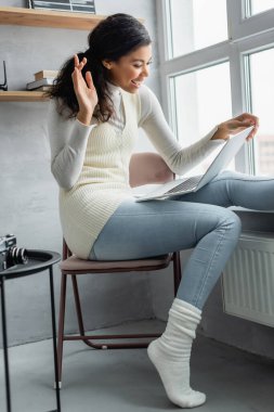 Mutlu Afro-Amerikalı kadın evdeki bilgisayar başında el sallıyor.