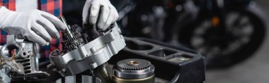 Parçalanmış motorsiklet vites kutusu ve pankartı kontrol eden eldivenli tamirci görüntüsü.
