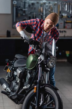 Kareli gömlekli ve eldivenli tamirci motosiklet gidonunda fren kolunu inceliyor.